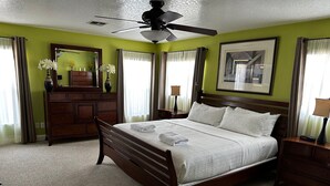 A hotel room with a bed, a dresser, a vanity with a mirror, a ceiling fan, and a framed picture on the wall.