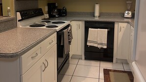 A compact kitchen with white cabinets, a stove, microwave, and a ceiling fan.