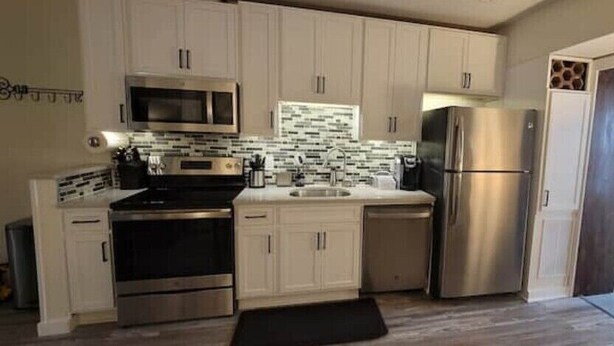 A compact kitchen with white cabinets, stainless steel appliances, and a tiled backsplash.