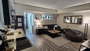 A modern living room with a sofa, coffee table, and a bean bag. There is a TV, a lamp, and a clock on the wall.