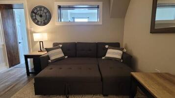 Un dormitorio acogedor con un sofá cama marrón oscuro, una mesita de noche pequeña, una lámpara y un reloj en la pared.
