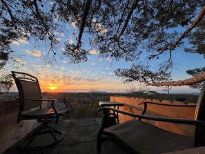 En terrasse med to stole og et bord, der udover et smukt landskab med solnedgang.