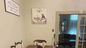 A dining area with a wooden table and white chairs, a chandelier, and a painting on the wall.
