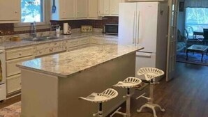 A kitchen with white cabinets, a central island with stools, a ceiling fan, and a clock on the wall.