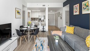 Un salon moderne avec un canapé gris, des fauteuils noirs, une table basse et un téléviseur.