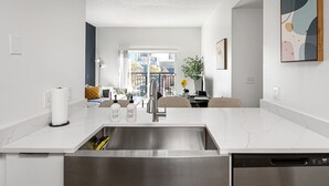 Une cuisine moderne dotée d’un évier en acier inoxydable, de plans de travail blancs et d’un lave-vaisselle encastré.