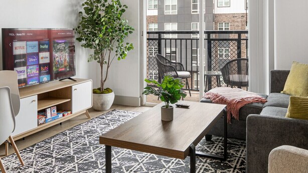 A modern living room with a TV, a coffee table, a sofa, and a balcony with chairs. - Urban Retreat | Free WiFi+Parking, Walk to Stadium (Charlotte)