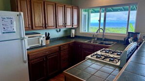 Una cocina con armarios de madera, microondas, estufa a gas y ventana con vista al océano.