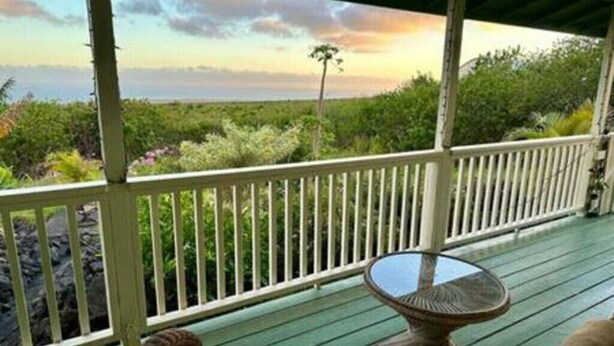 Un espacio al aire libre techado con terraza de madera, mobiliario de mimbre y vista al paisaje.
