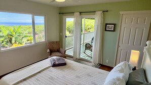 Un dormitorio con cama, una silla, un balcón con vista al océano y una puerta.