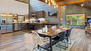 A modern kitchen with stainless steel appliances, a dining area with a wooden table and chairs, and a large window offering a view of the outdoors. - Escape to Elegance by Ghosal Luxury Lodging (Sevierville)