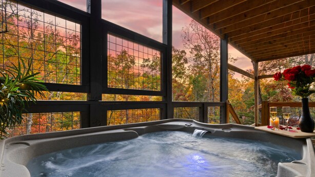 A hot tub with a wooden deck and a glass enclosure, surrounded by autumn foliage. - Escape to Elegance by Ghosal Luxury Lodging (Sevierville)