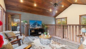 A cozy living room with a wooden ceiling, a mounted TV, a dining table with a cowhide rug, and a balcony with a wooden railing. - Escape to Elegance by Ghosal Luxury Lodging (Sevierville)