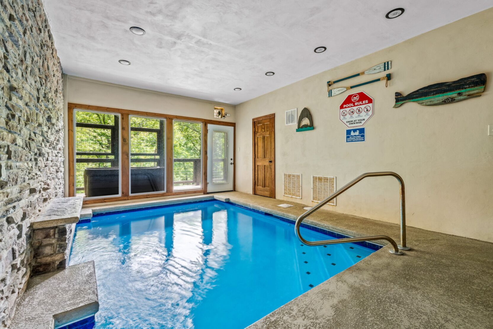 Une piscine intérieure à l’eau d’un bleu cristallin, avec une terrasse en bois et un mur en pierre.
