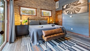 A bedroom with a brick wall, a bed with a bench, a window, and a wall-mounted artwork. - Escape to Elegance by Ghosal Luxury Lodging (Sevierville)