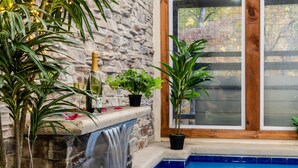 A stone wall with a small waterfall, a pool, and potted plants. - Escape to Elegance by Ghosal Luxury Lodging (Sevierville)