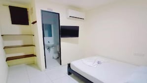 Una habitación pequeña y limpia con cama, mesita de noche, televisor montado en la pared y aire acondicionado.