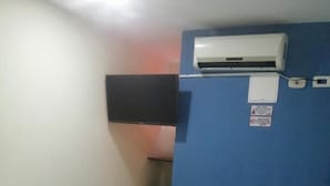 Una habitación de hotel con cama, pared azul, equipo de aire acondicionado y un estante pequeño.