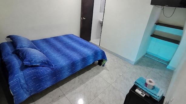Un dormitorio con una cama, un equipo de aire acondicionado, un televisor y una mesita con objetos encima.