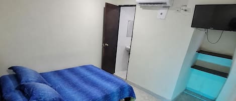 A bedroom with a bed, an air conditioning unit, a television, and a small table with items on it.