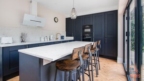 A modern kitchen with dark cabinets, a large island, bar stools, and a view through a glass door.