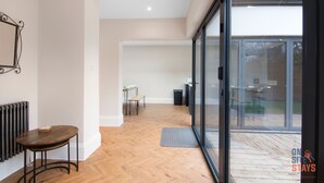 A modern interior with a wooden floor, a glass door leading to an outdoor area, and a small table with a chair.