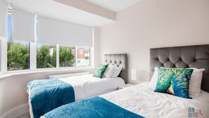 A bedroom with two beds, white bedding, and a window with a view of houses and trees.