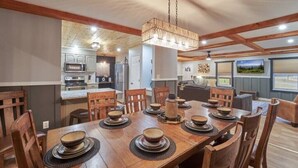 A dining area with a wooden table set for six, surrounded by chairs. A chandelier hangs above, and the room has exposed wooden beams on the ceiling. - ENTERTAINMENT GALORE!NEWLY UPGRADED -GREAT LOCATION, CLOSE TO MAJOR ATTRACTIONS! (Sevierville)