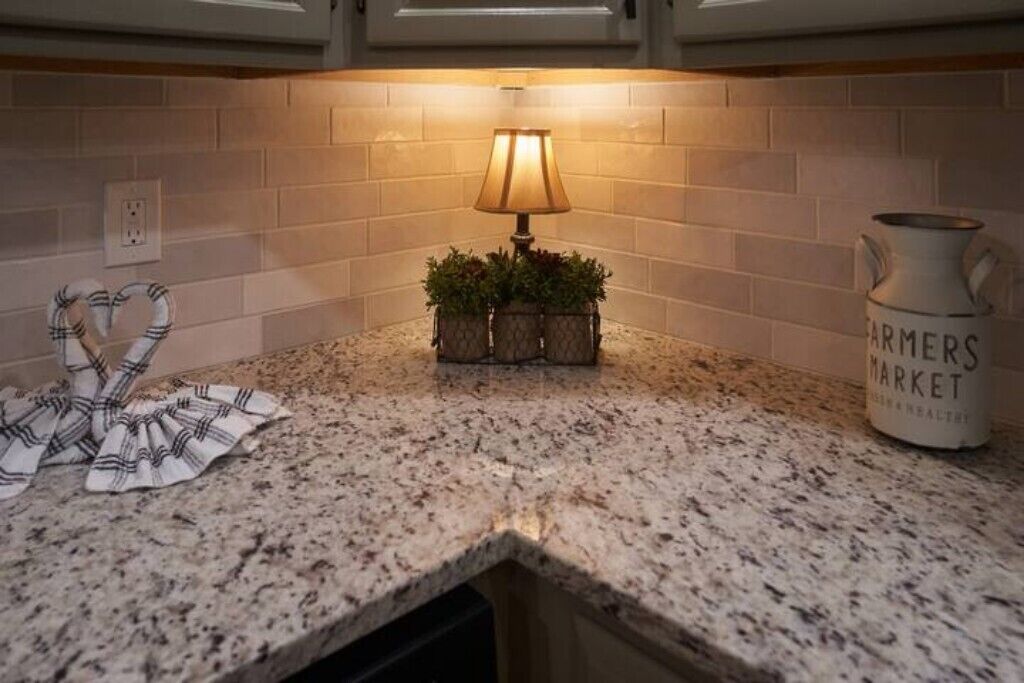 A kitchen counter with a granite top, a small table lamp, a potted plant, a cloth, and a pitcher labeled "Farmers Market".