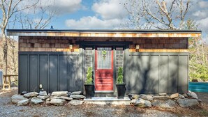 Una pequeña construcción de madera con una puerta roja, rodeada de rocas y grava.