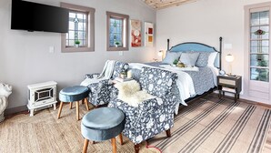 Un dormitorio con cama, dos mesitas de noche, televisor y chimenea.