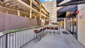 An outdoor seating area with a long table and chairs, a metal railing, and a building with a sign that reads "Place Suites." - 3BR Loft Near Convention Center + Breakfast + Pool (Dallas)