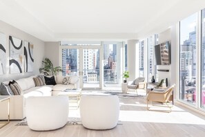 A modern living room with a white sofa, a coffee table, and a large window offering a city view. - Luxury Loft Collection 01 - Terrace - River North (Chicago)