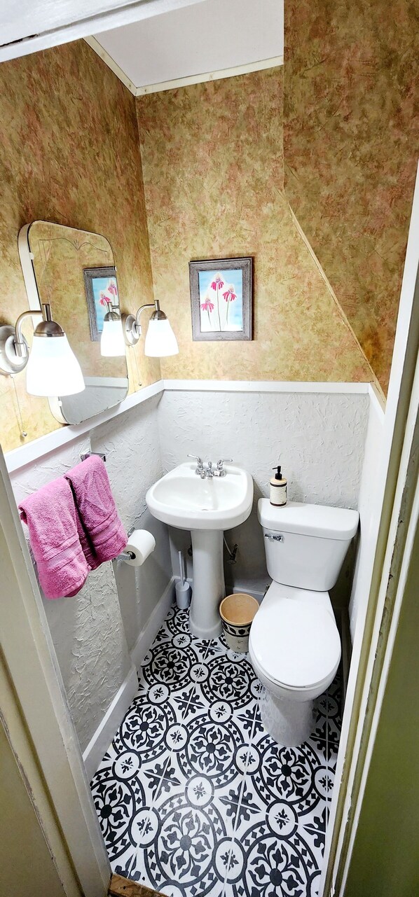 A bathroom with a white sink, toilet, and bathtub. There are two pink towels hanging on the wall and a framed picture above the sink.