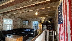 A rustic living room with exposed wooden beams, a black leather sofa, a wooden coffee table, and a bookshelf. - Washington Family Home - National Treasure, Est 1750 located at 107 S Lee Street (Alexandria)