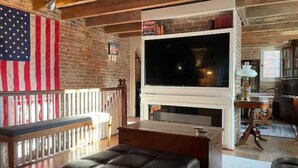 A living room with a fireplace, a large flat-screen TV, a bench, and an American flag. - Washington Family Home - National Treasure, Est 1750 located at 107 S Lee Street (Alexandria)