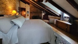 A cozy attic bedroom with a large bed, a chair, a small table, and a fireplace. - Washington Family Home - National Treasure, Est 1750 located at 107 S Lee Street (Alexandria)