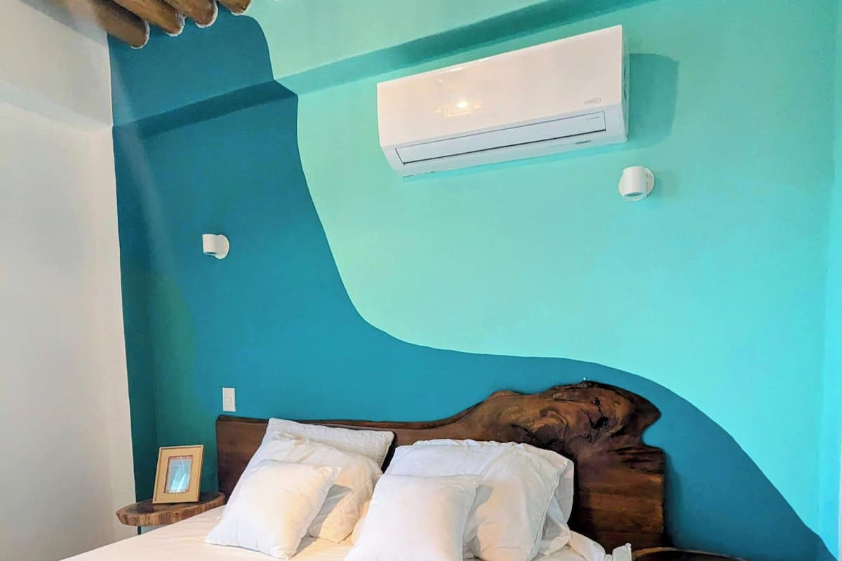 A bedroom with a wooden headboard, a bed with white bedding, a nightstand with a framed photo, and a small stool.