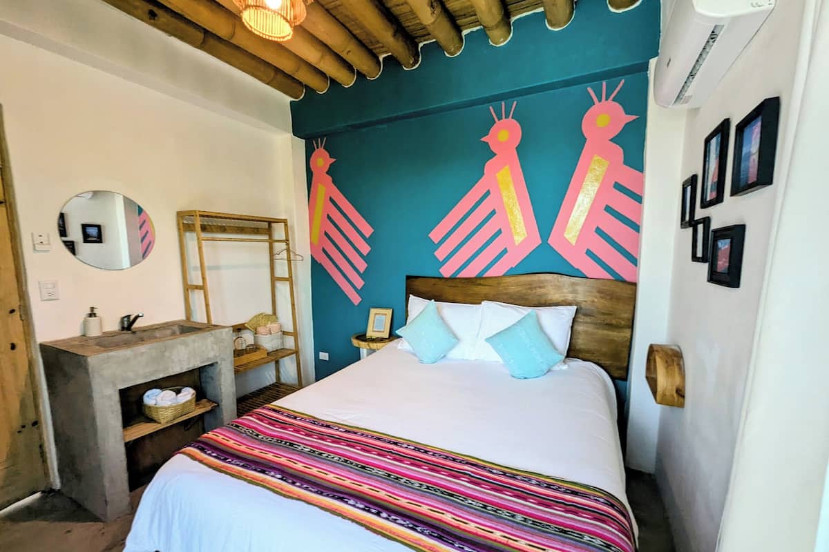 A bedroom with a bed, a wooden headboard, a mirror, a bedside table, and a wall with a geometric design.