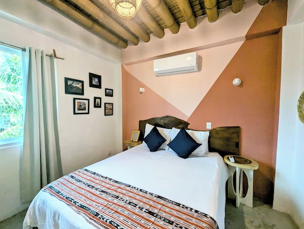 Un dormitorio con cama, mesita de noche, aire acondicionado instalado en la pared y cuadros enmarcados.