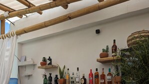 Une pièce avec un plafond en bambou, des étagères en bois où sont disposées des bouteilles et des plantes, un distributeur d’eau et un panneau sur lequel on peut lire « Wander » (qui signifie « Explorez » ou « Laissez-vous guider »).
