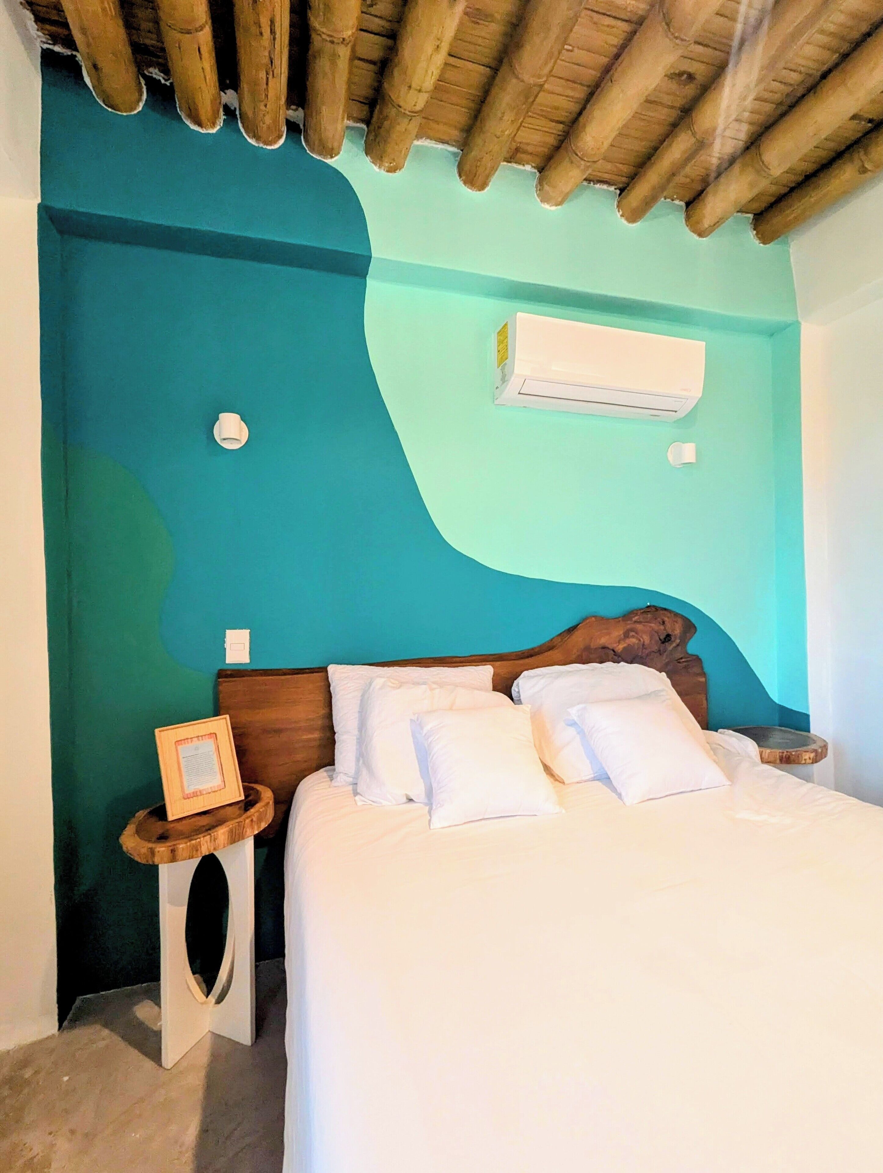 Un dormitorio con una cama, cabecera de madera, una mesita de noche pequeña y un equipo de aire acondicionado en la pared.