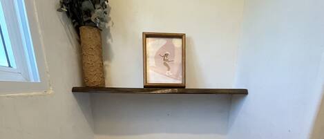 Une petite salle de bain avec des toilettes, une étagère sur laquelle est posée une photo encadrée et un rouleau de papier toilette.