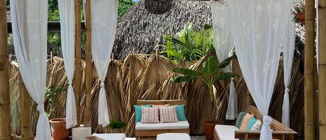 Un área de estar al aire libre cubierta con mobiliario de madera y toldos blancos.