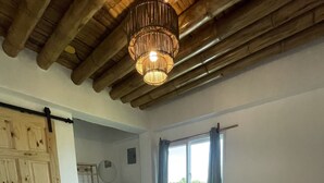A bedroom with a large bed, a wooden ceiling, a window with curtains, and a door.