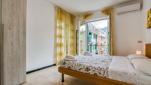 A bedroom with a bed, a window with yellow curtains, and a view of colorful buildings outside. - 2 bedroom awesome apartment in Moneglia (Moneglia)