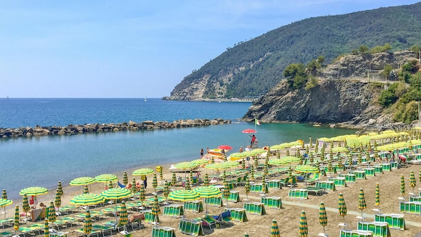 A beach with numerous sun umbrellas and lounge chairs, a rocky coastline, and a sailboat in the distance. - 2 bedroom awesome apartment in Moneglia (Moneglia)