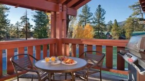 Un espacio al aire libre cubierto con una mesa para dos, una parrilla y vistas a árboles y una montaña.