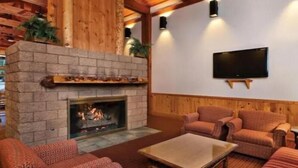 Una sala de estar acogedora con chimenea de piedra, paredes de madera y televisor de pantalla plana montado en la pared.