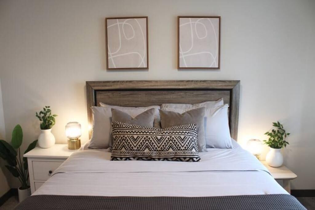 A neatly made bed with patterned pillows, a wooden headboard, and two wall art pieces above it.